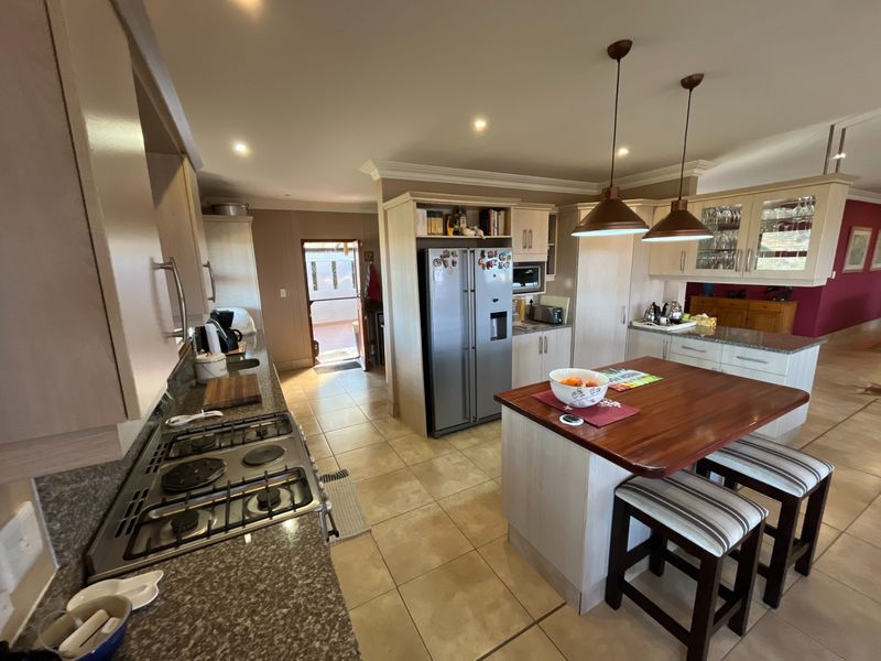 Spacious kitchen featuring granite countertops, a central island with breakfast seating, gas hob, and ample built-in cabinetry with modern pendant lighting.