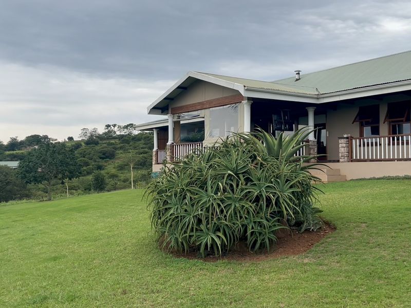 A view of the rear elevation featuring a covered patio with timber railings, stone accents, and a well-maintained lawn overlooking the surrounding landscape.