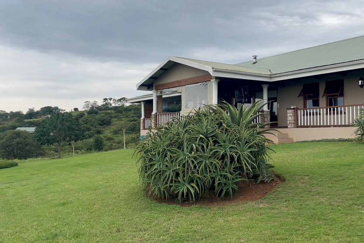 A view of the rear elevation featuring a covered patio with timber railings, stone accents, and a well-maintained lawn overlooking the surrounding landscape.