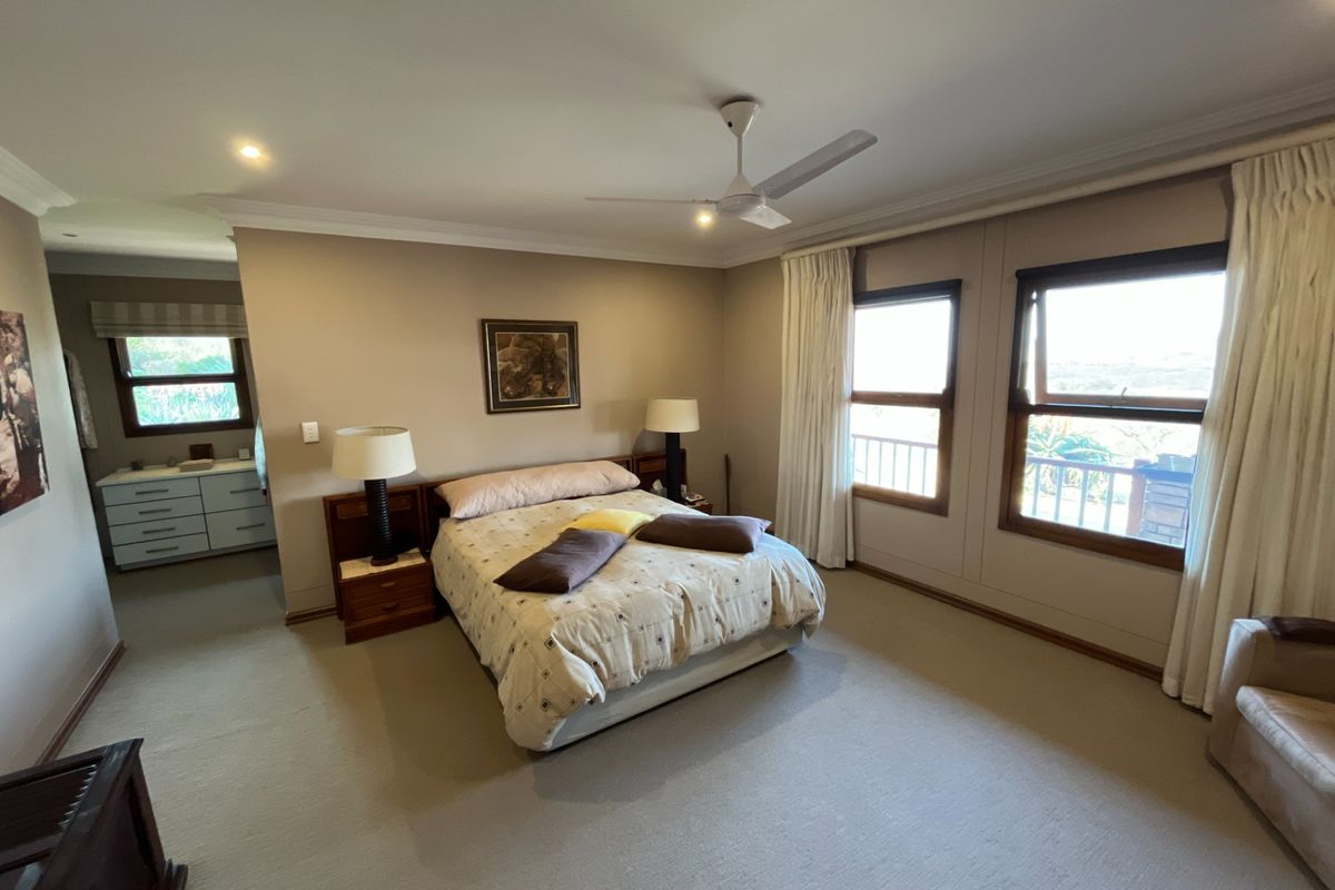 Spacious bedroom featuring neutral carpeting, a ceiling fan, and an adjoining vanity area with natural light from large windows.