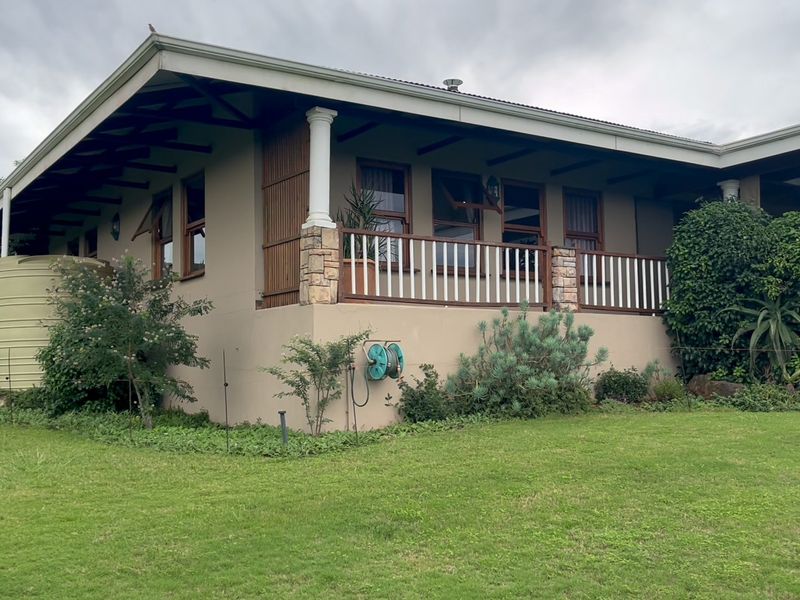 Rear view of the house featuring a covered patio with stone-clad pillars, timber roof trusses, and a large water tank set in a garden.