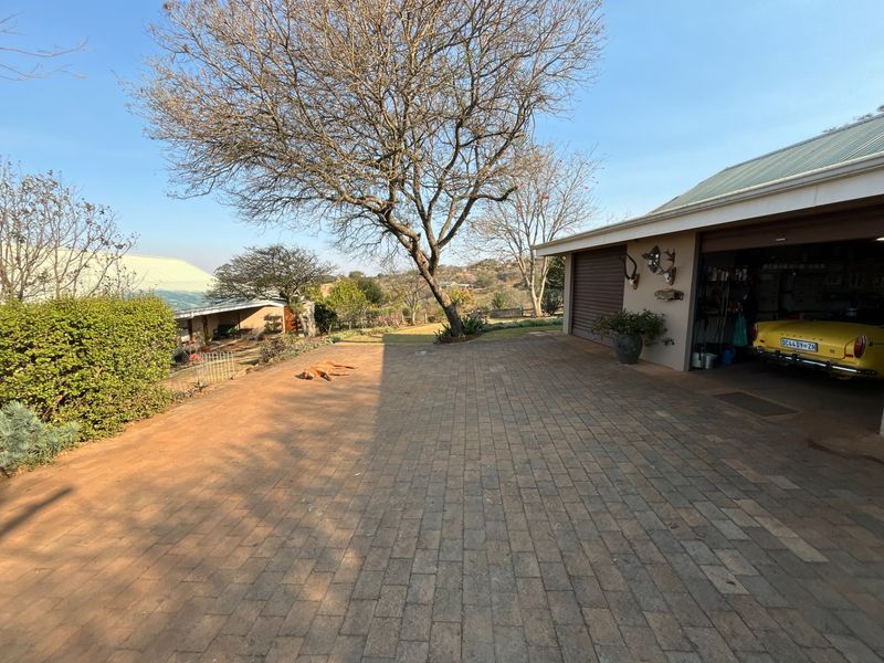 A paved driveway leading to a garage with a metal door, set against a backdrop of mature trees and open landscape.