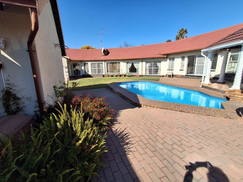 Rear courtyard featuring a swimming pool, brick paved patio area, and access to the main house under a tiled roof.