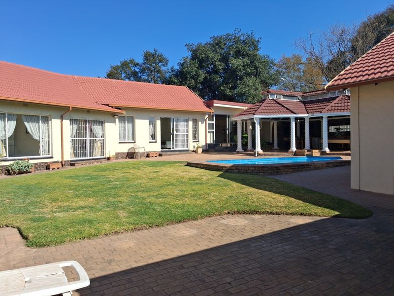 Rear exterior view featuring a swimming pool, paved patio area, lawn, and a covered entertainment space with a tiled roof.