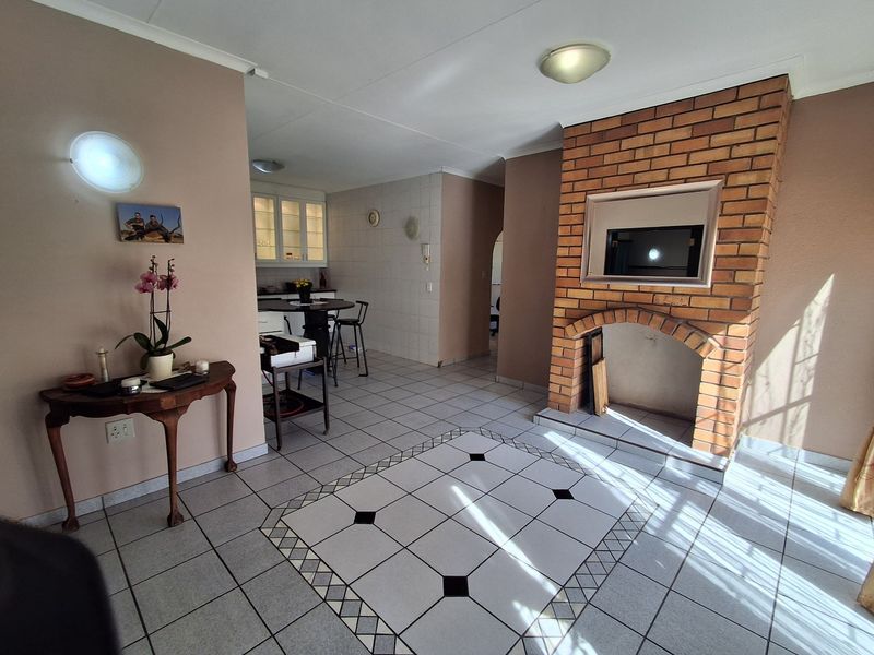 Open plan living area featuring tiled flooring and a prominent brick fireplace, with a view towards the kitchen area.