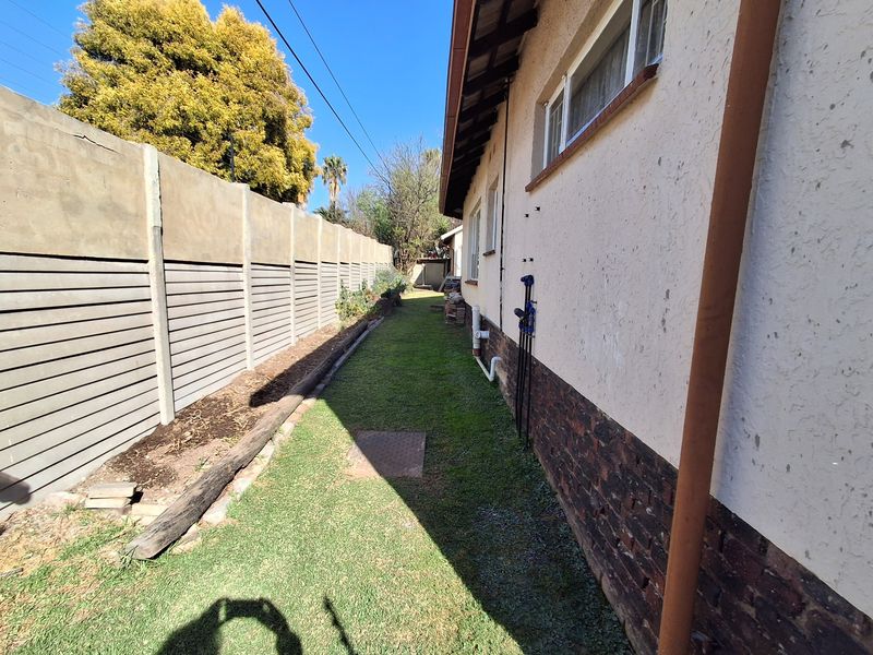 A narrow side garden area featuring a precast concrete boundary wall, lawn, and exterior brick and plaster wall finishes.
