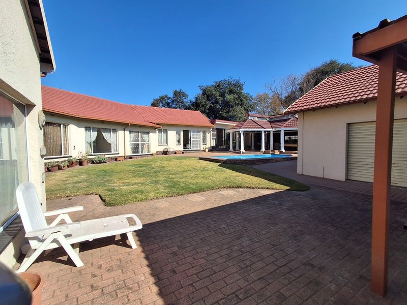 Spacious rear garden featuring a paved patio, well-maintained lawn, swimming pool, and a covered gazebo area, perfect for outdoor entertaining.