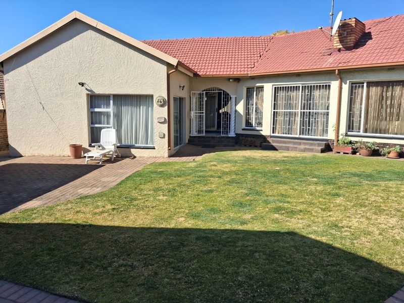 Rear view of the house featuring a paved patio area, lawn, and secure access points with security gates and bars.