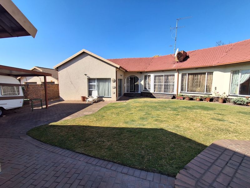Rear view of the house featuring a paved patio area, a lawn, and a carport structure.