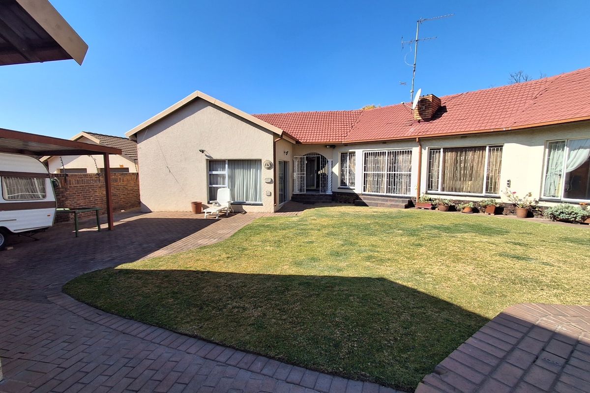Rear view of the house featuring a paved patio area, a lawn, and a carport structure.
