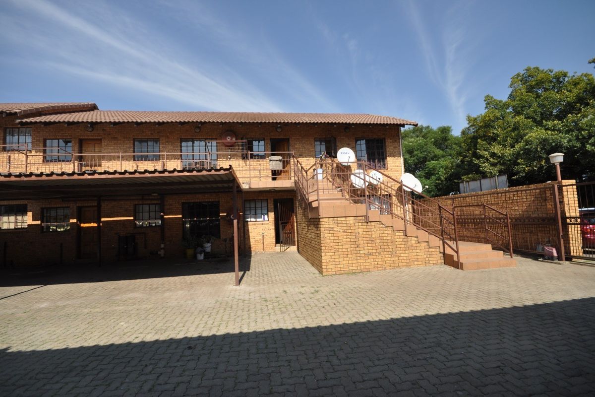 Rear view of a two-story face brick commercial building featuring a paved parking area, carport, and external staircase access to the upper level.