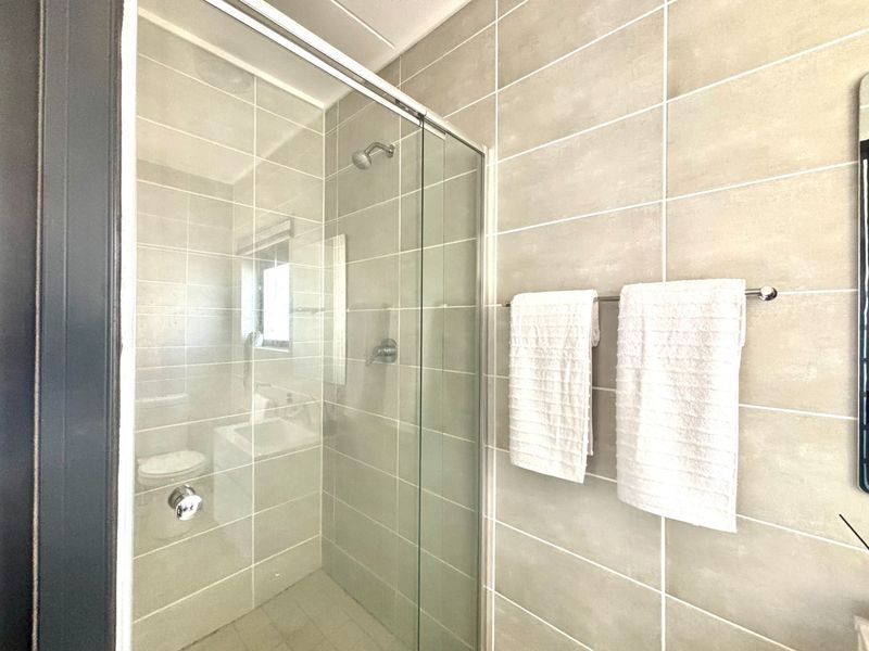 A modern bathroom featuring a glass-enclosed shower with neutral ceramic wall tiling and a fixed towel rail.