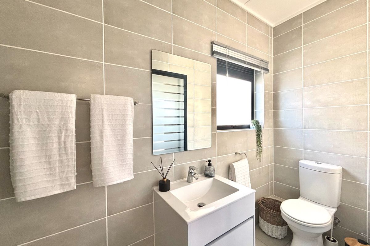A modern, well-maintained bathroom featuring neutral wall tiles, a contemporary vanity with basin, and a toilet.