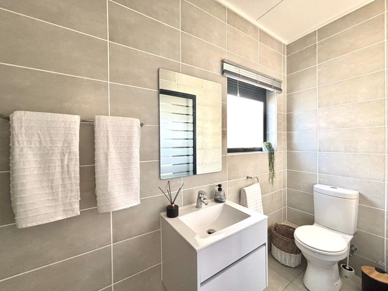 A modern, well-maintained bathroom featuring neutral wall tiles, a contemporary vanity with basin, and a toilet.