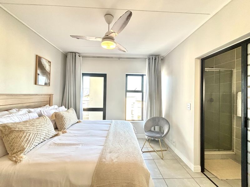A well-maintained bedroom featuring tiled flooring, a ceiling fan, and an integrated en-suite bathroom with a glass shower enclosure.