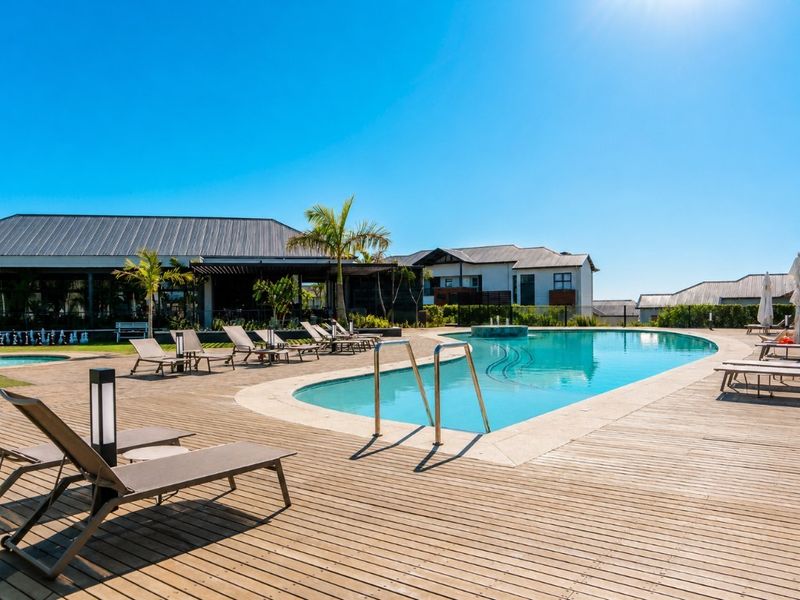 A well-maintained outdoor swimming pool area featuring timber decking, a water feature, and surrounding landscaped grounds within a residential complex.