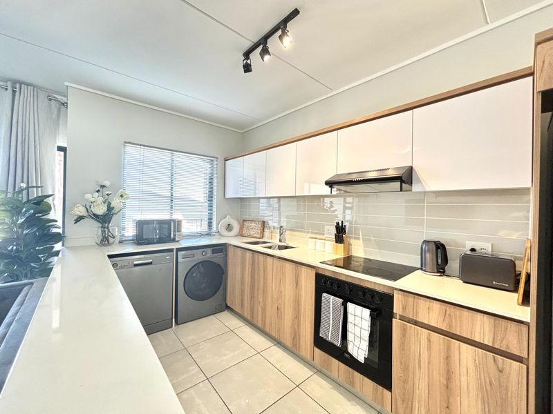Modern kitchen featuring wood-grain cabinetry, sleek white upper cabinets, integrated appliances, tiled backsplash, and durable ceramic flooring with efficient track lighting.