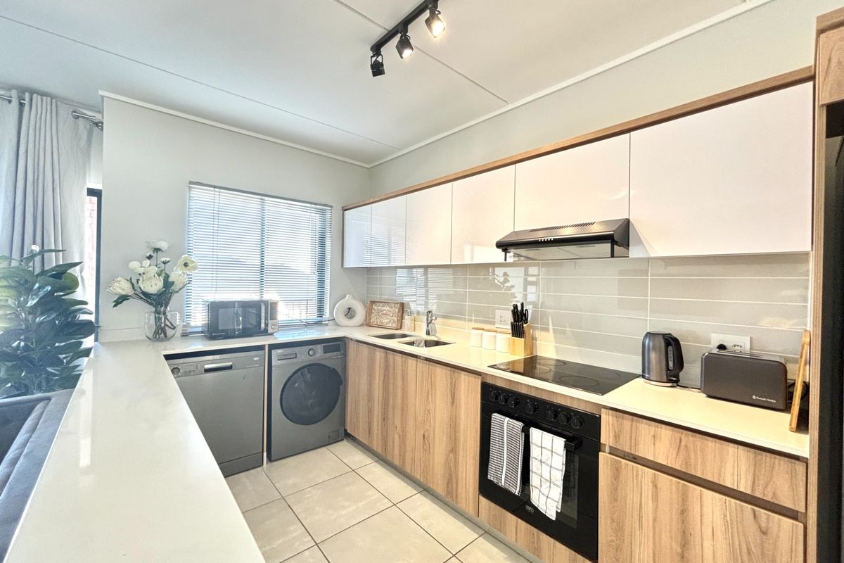 Modern kitchen featuring wood-grain cabinetry, sleek white upper cabinets, integrated appliances, tiled backsplash, and durable ceramic flooring with efficient track lighting.