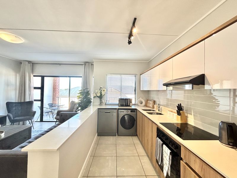 Modern open-plan kitchen and living area featuring sleek cabinetry, integrated appliances, tiled flooring, and direct access to a private balcony.