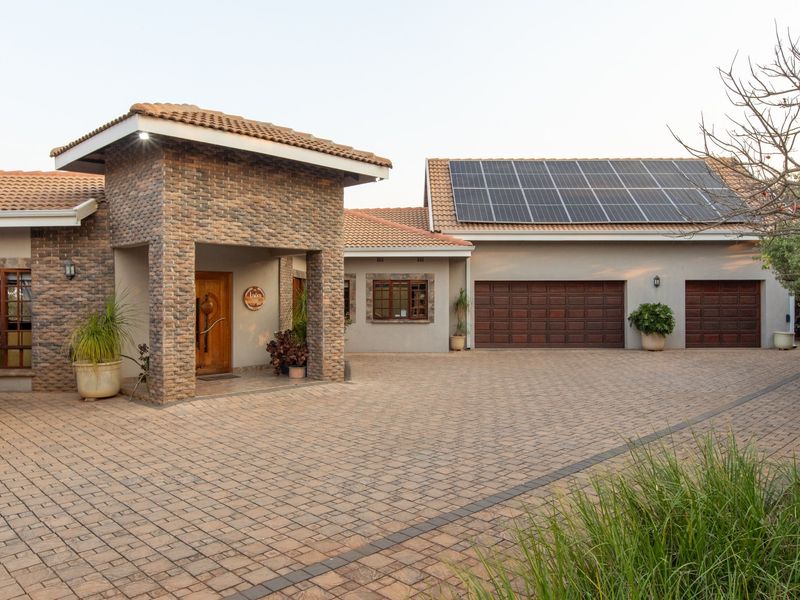 A well-maintained front elevation featuring a brick facade, covered entrance, paved driveway, and a double garage equipped with roof-mounted solar panels.