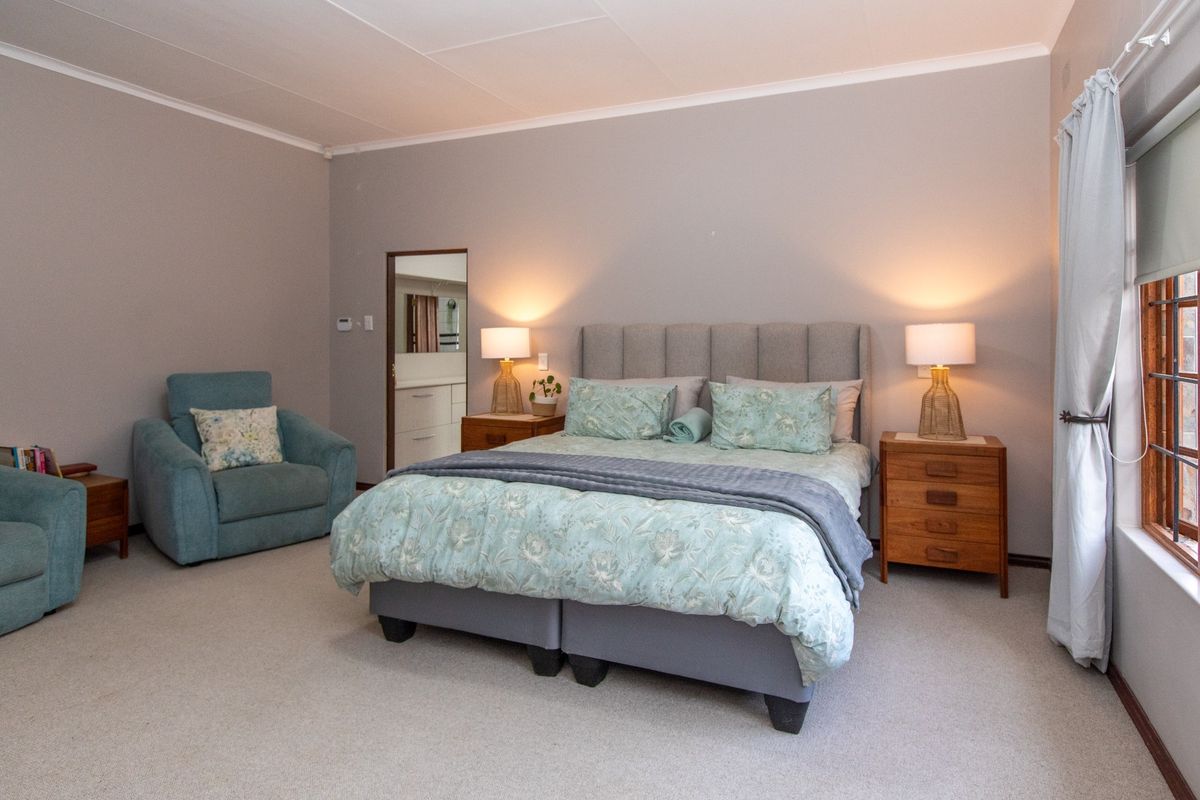 A spacious bedroom featuring neutral wall tones, carpeted flooring, and a window with roller blinds, offering a comfortable and well-maintained living space.