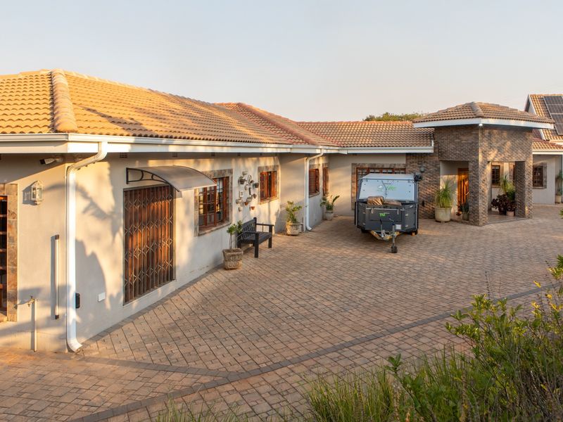 Spacious paved driveway leading to a well-maintained single-story residence featuring stone accents, tiled roofing, and integrated solar panels.