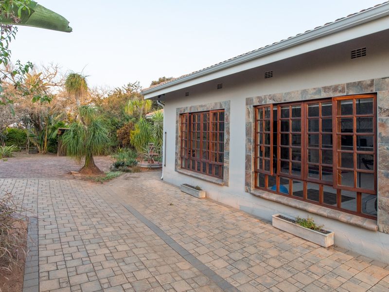 Rear exterior view featuring a paved patio area, stone-trimmed timber-framed windows, and a well-maintained garden setting.