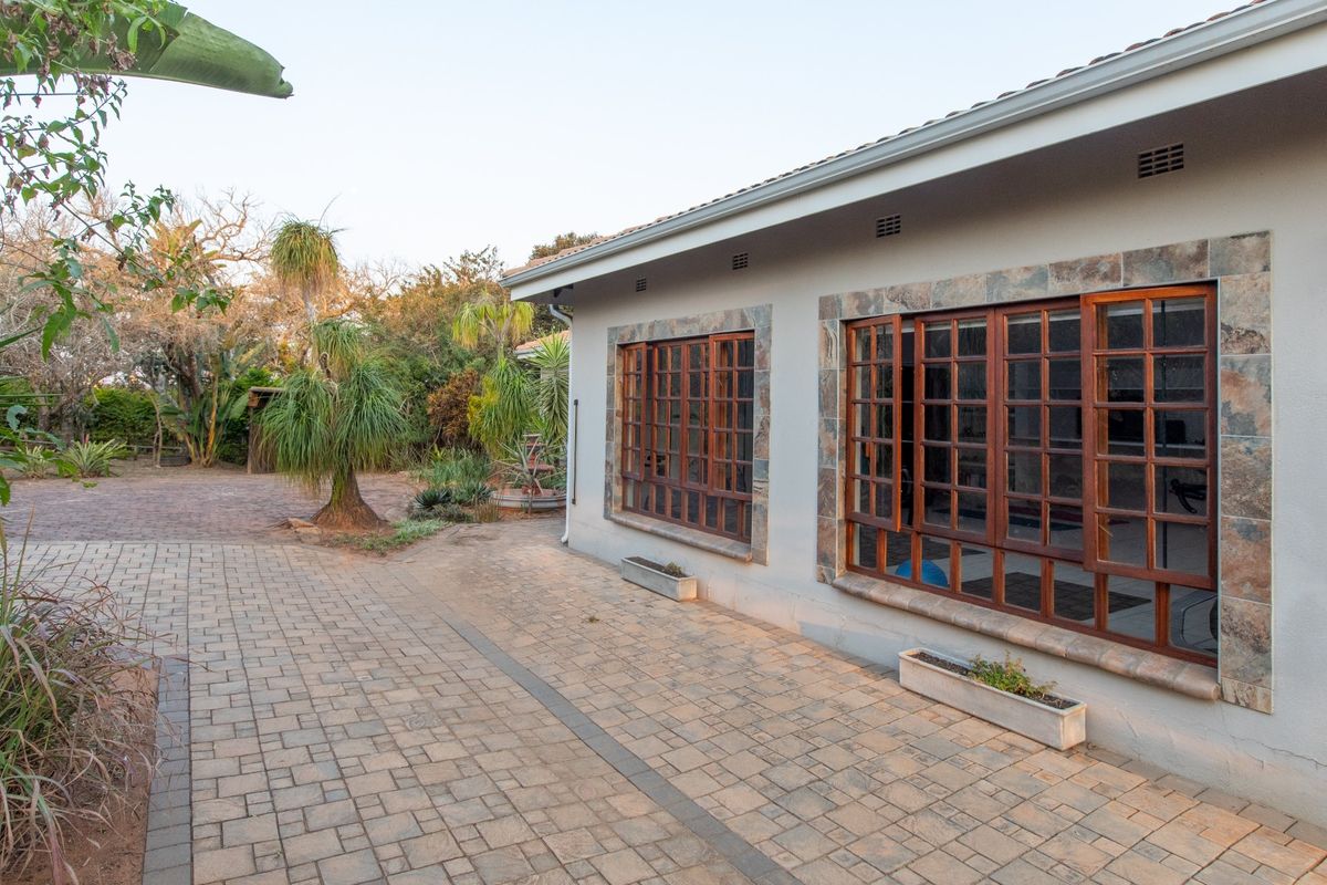 Rear exterior view featuring a paved patio area, stone-trimmed timber-framed windows, and a well-maintained garden setting.