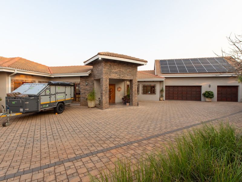 Spacious front exterior featuring a paved driveway, double garage, stone-clad entrance portico, and roof-mounted solar panels.