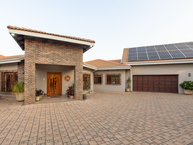 Front elevation of a well-maintained house featuring stone cladding, a paved driveway, timber entrance door, and roof-mounted solar panels.