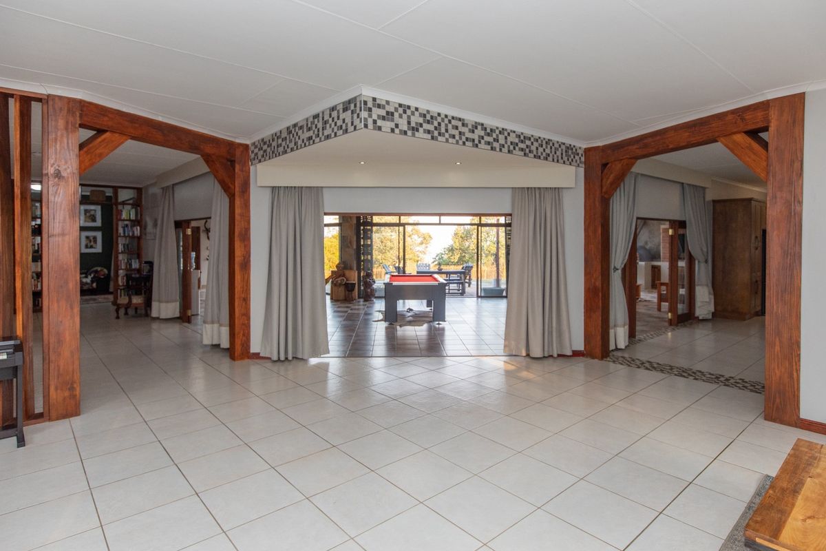 Spacious open-plan living area featuring large timber support beams, neutral tiled flooring, and expansive sliding glass doors leading to an outdoor patio.