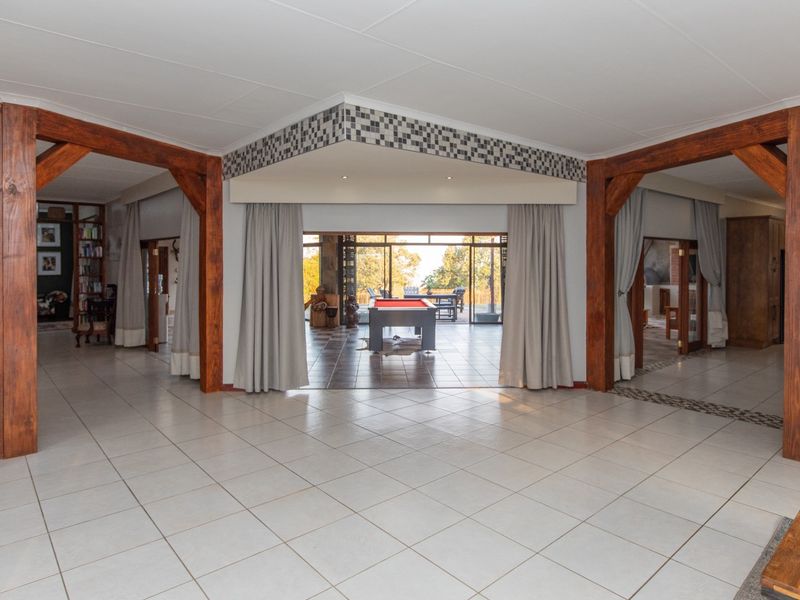 Spacious open-plan living area featuring large timber support beams, neutral tiled flooring, and expansive sliding glass doors leading to an outdoor patio.