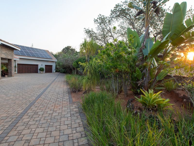 A well-maintained front exterior featuring a paved driveway, double garage with solar panels, and established garden landscaping at sunset.