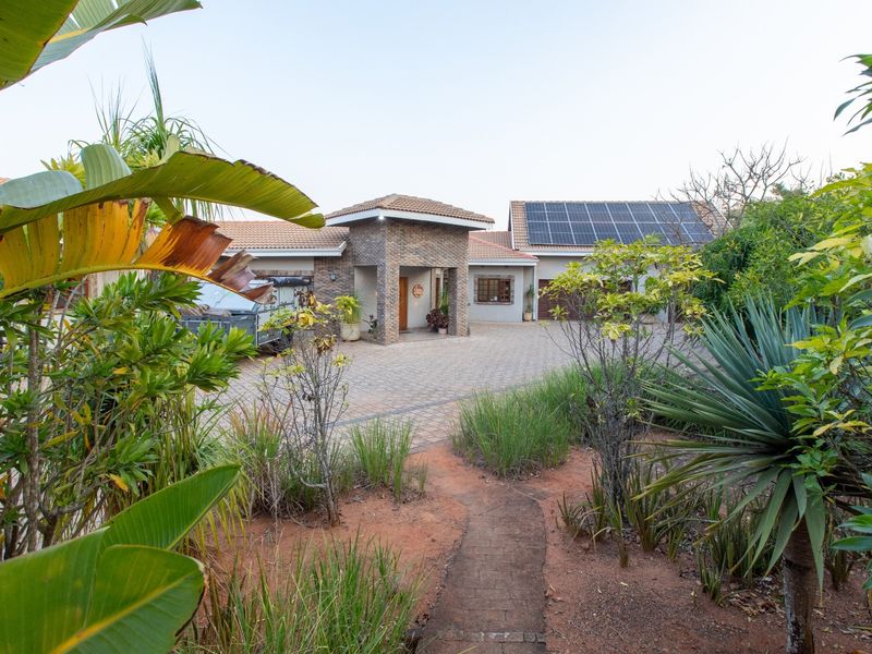 Front view of a well-maintained house featuring a paved driveway, stone-clad entrance, and roof-mounted solar panels set within a landscaped garden.