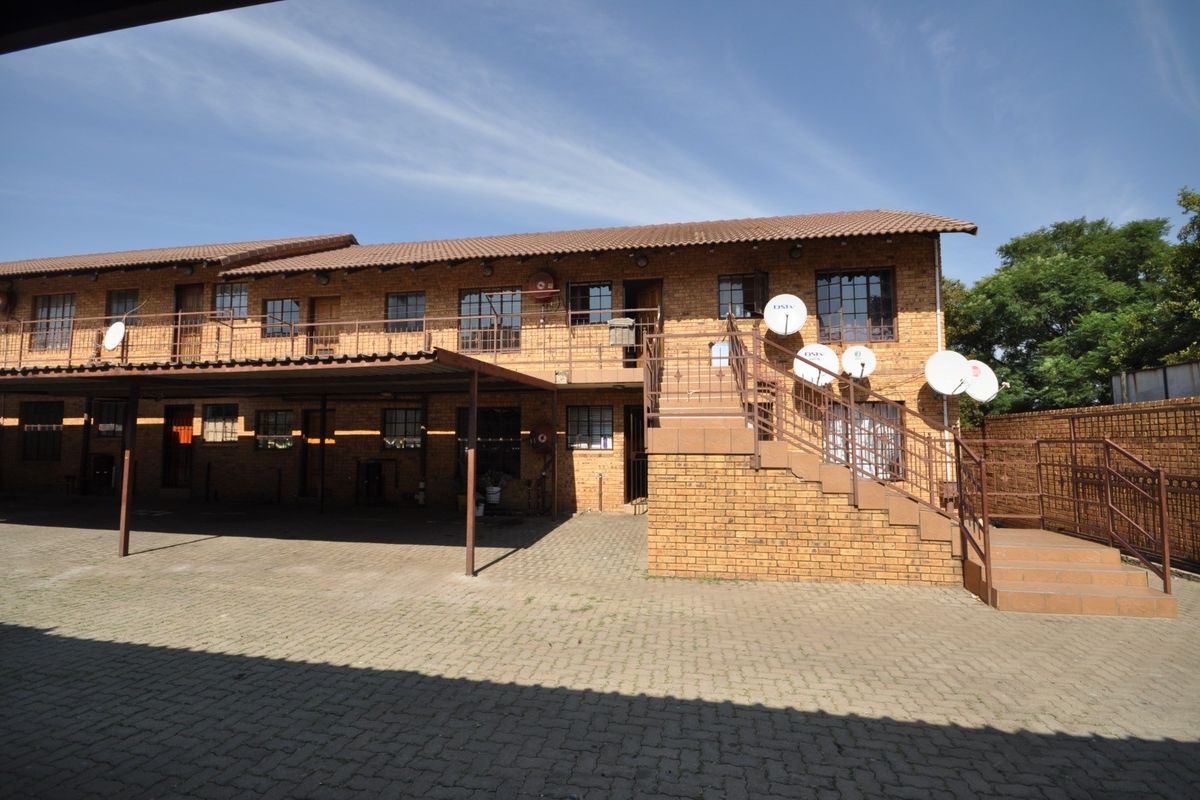 Exterior view of a multi-story face brick commercial building featuring a paved driveway, covered carport, and external staircase access to the upper level.