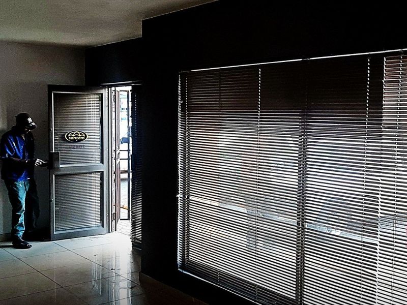 An empty commercial entry area featuring tiled flooring, large windows with venetian blinds, and an aluminium framed glass entrance door.