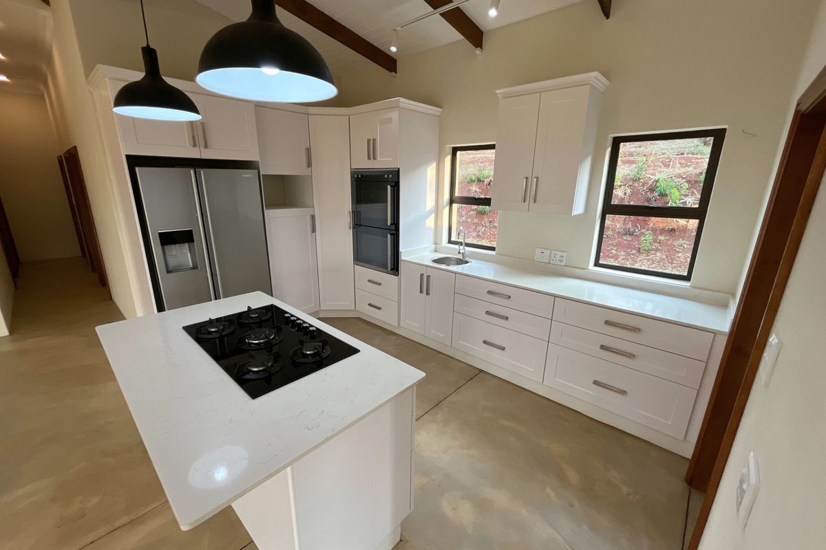 Modern kitchen featuring white shaker cabinetry, quartz countertops, a central island with a gas hob, built-in double oven, and exposed timber ceiling beams.