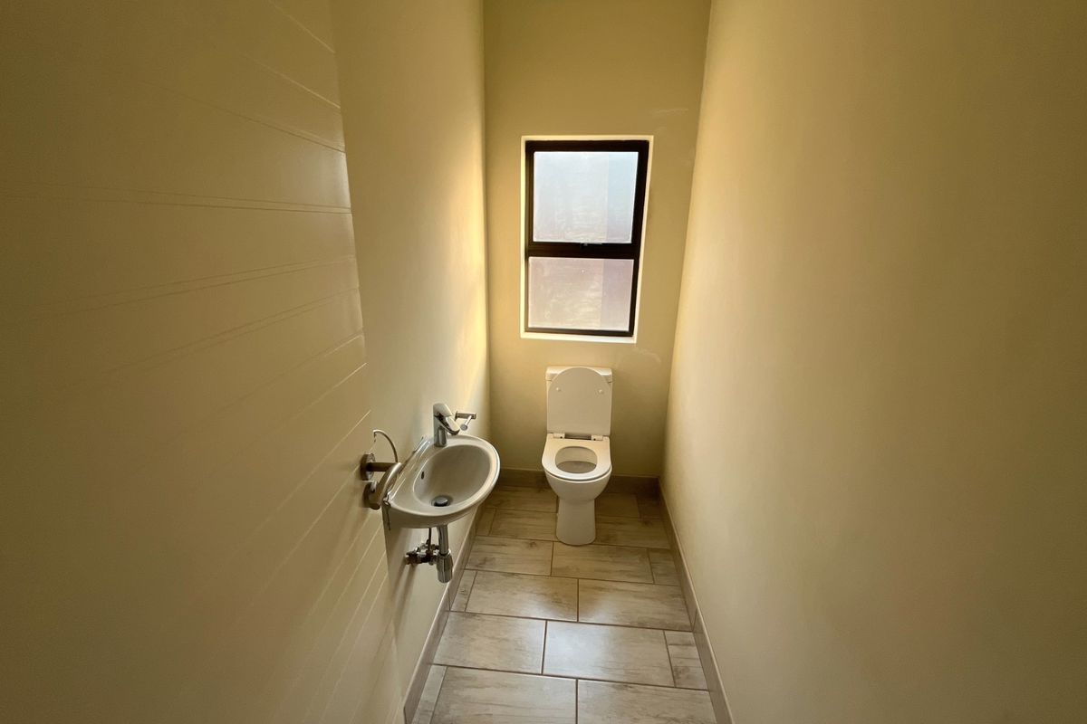 A compact, clean guest bathroom featuring a wall-mounted basin, toilet, and neutral tiled flooring with natural light from a window.