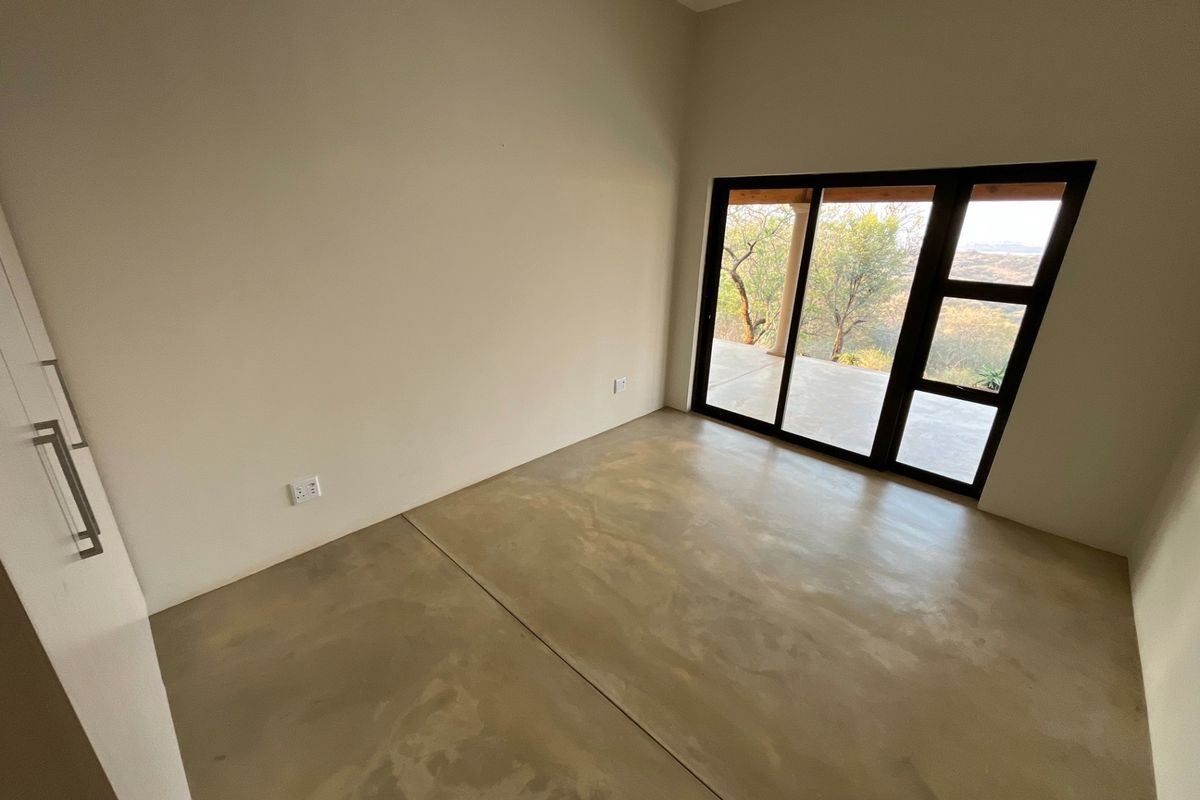 A bright, empty bedroom featuring polished concrete floors, a built-in cupboard, and a sliding glass door providing access to an outdoor patio area.