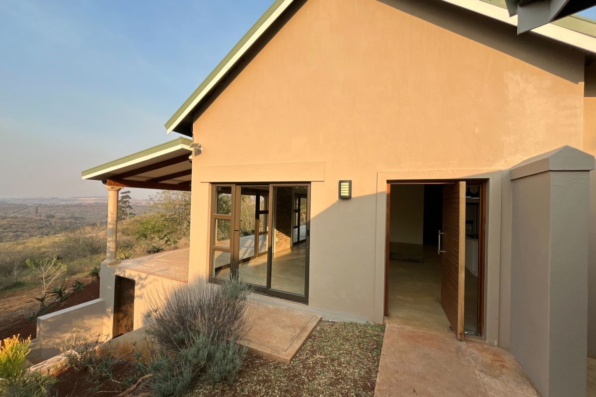 Rear elevation of the house featuring a covered patio, sliding glass doors, and a timber entrance door overlooking the surrounding landscape.