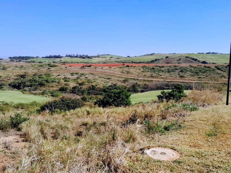 A scenic view overlooking a vast landscape with rolling hills, natural vegetation, and a glimpse of a golf course fairway.