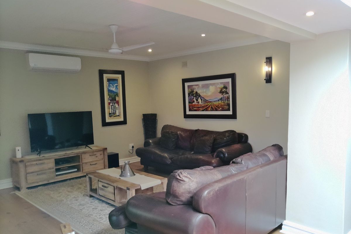 A comfortable living room featuring timber flooring, recessed downlighting, a ceiling fan, and a wall-mounted split-system air conditioner.