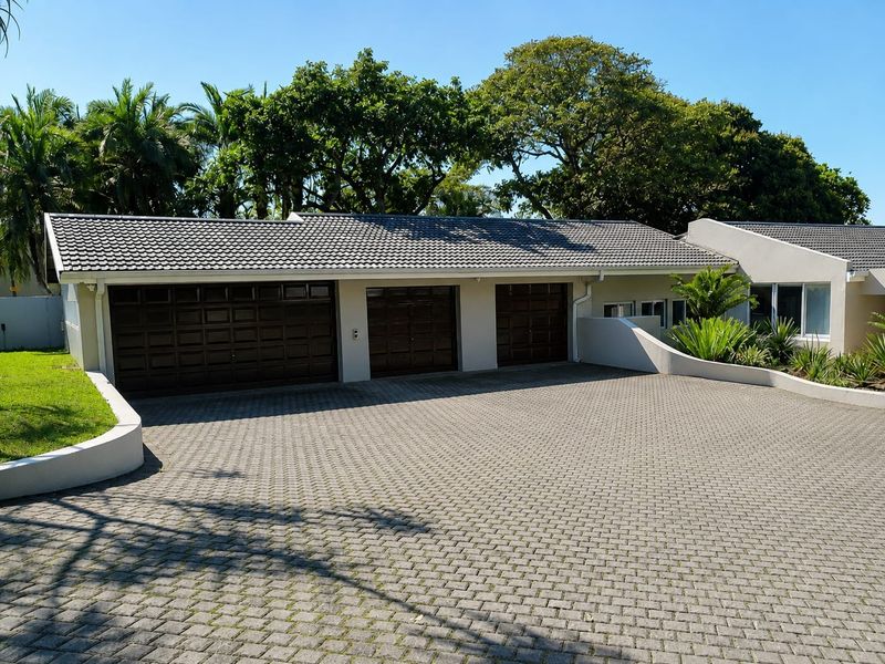 A well-maintained front exterior featuring a triple garage with dark panelled doors, a spacious paved driveway, and neat landscaping.