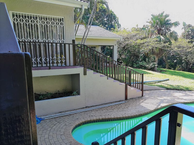 Outdoor pool area featuring brick paving, a built-in planter box, and a raised deck with metal security gates and railings overlooking the garden.