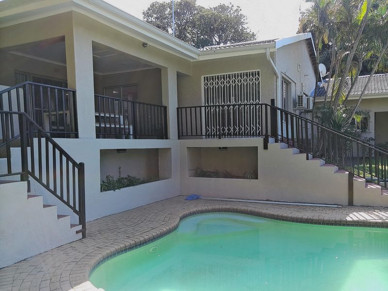 A well-maintained outdoor pool area featuring brick paving, a covered patio with metal railings, and built-in planters, providing a functional space for relaxation.