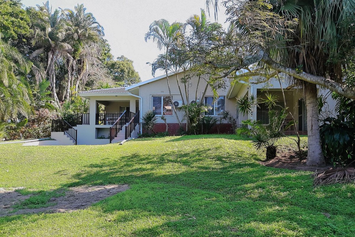 Rear view of the house featuring a covered patio, external staircase, and a spacious garden with mature trees.