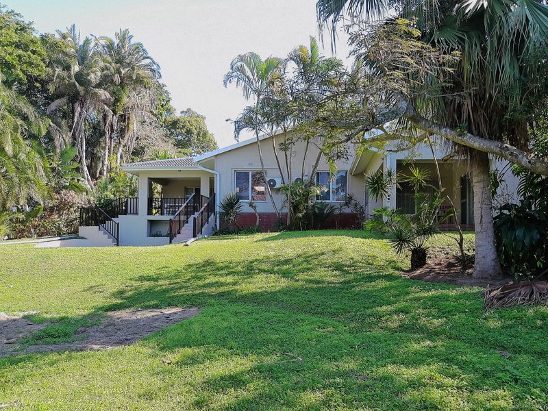 Rear view of the house featuring a covered patio, external staircase, and a spacious garden with mature trees.