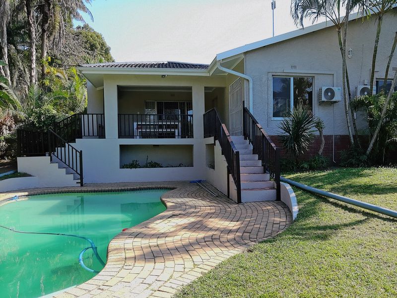 Rear exterior view featuring a swimming pool with paved surround, a covered patio area, and an external staircase leading to the main house level.