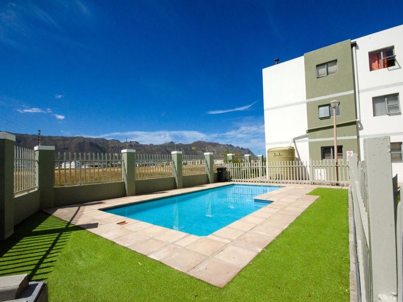 Communal swimming pool area featuring paved surround, artificial lawn, and perimeter fencing, set against a backdrop of mountain views.