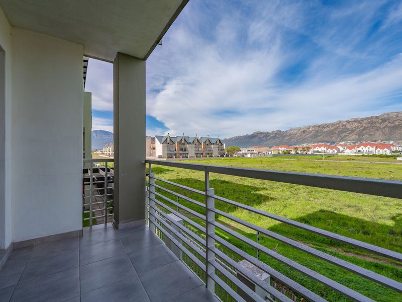 A spacious covered balcony featuring tiled flooring and a metal balustrade, offering expansive views of the surrounding landscape and mountains.